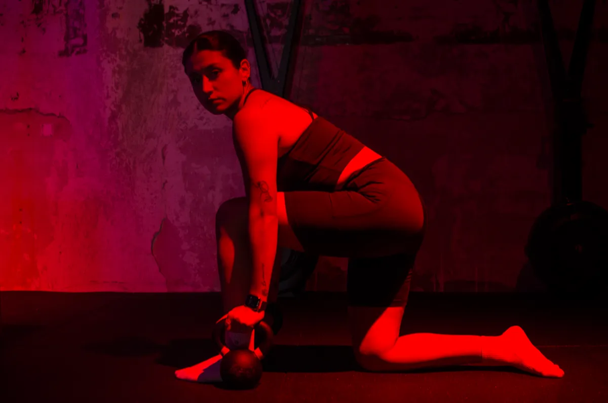Eli kneeling with a kettlebell under red studio light